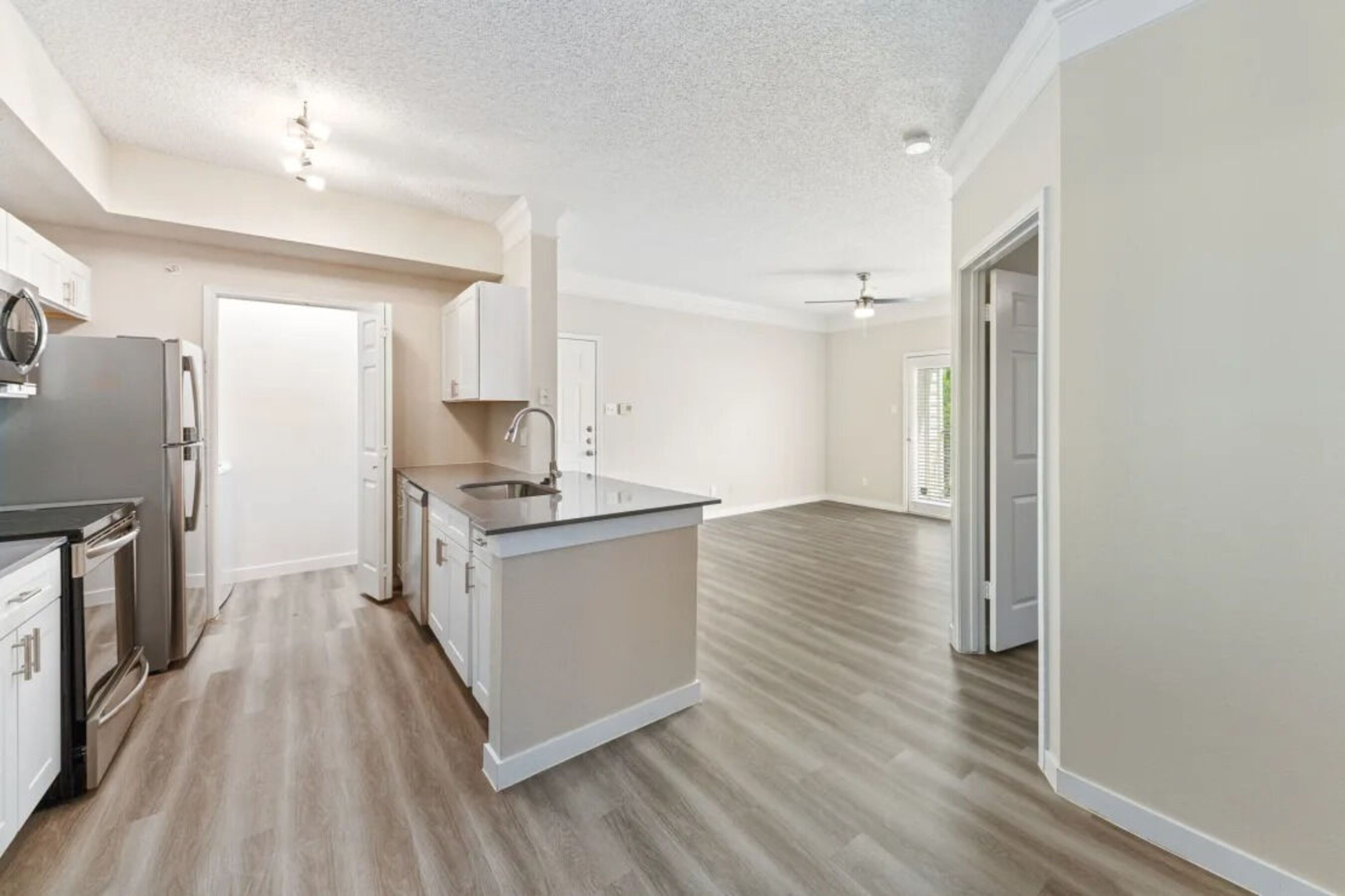 Open-concept kitchen and living room with stainless steel appliances and wood-style flooring at Alexi at Willow Bend